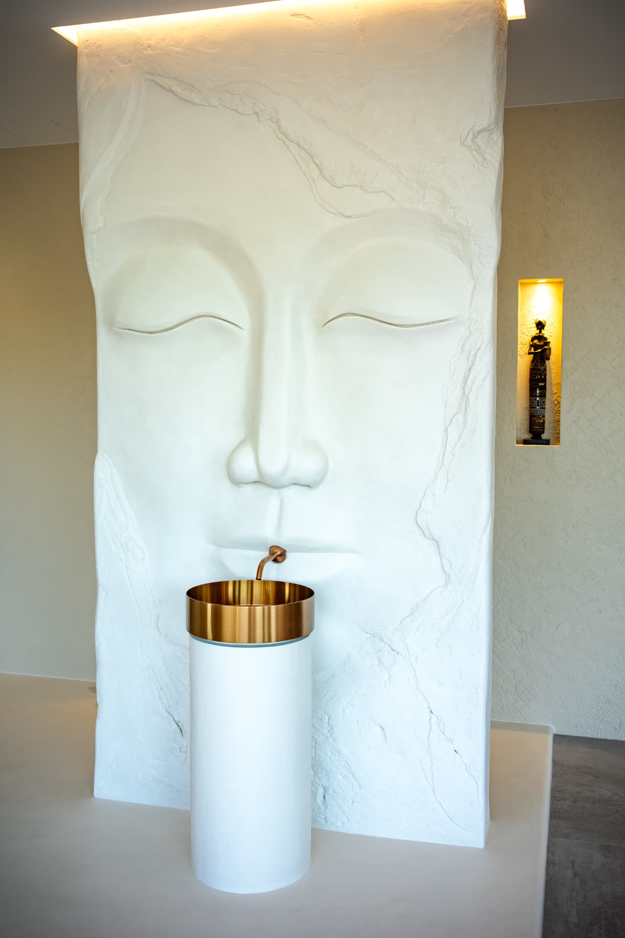 Skulpturale Stele mit reliefiertem Gesicht und zylindrischem Waschbecken im Schauraum